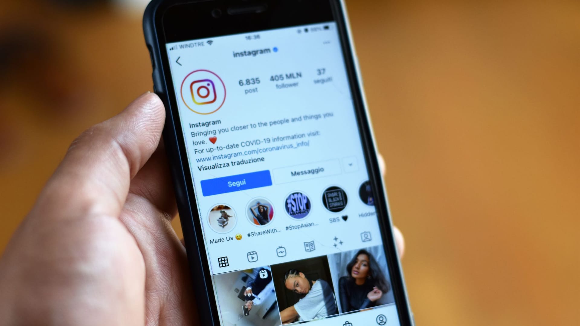Mão segurando um celular com um perfil de rede social aberto
